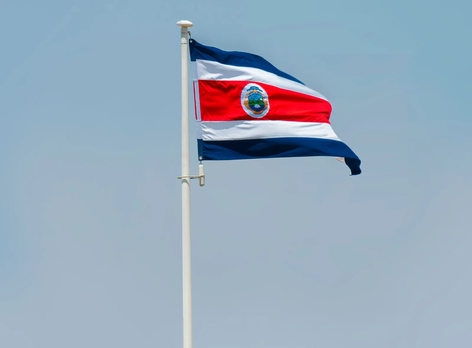 Bandera de Costa Rica ondeando en un asta contra el cielo azul.