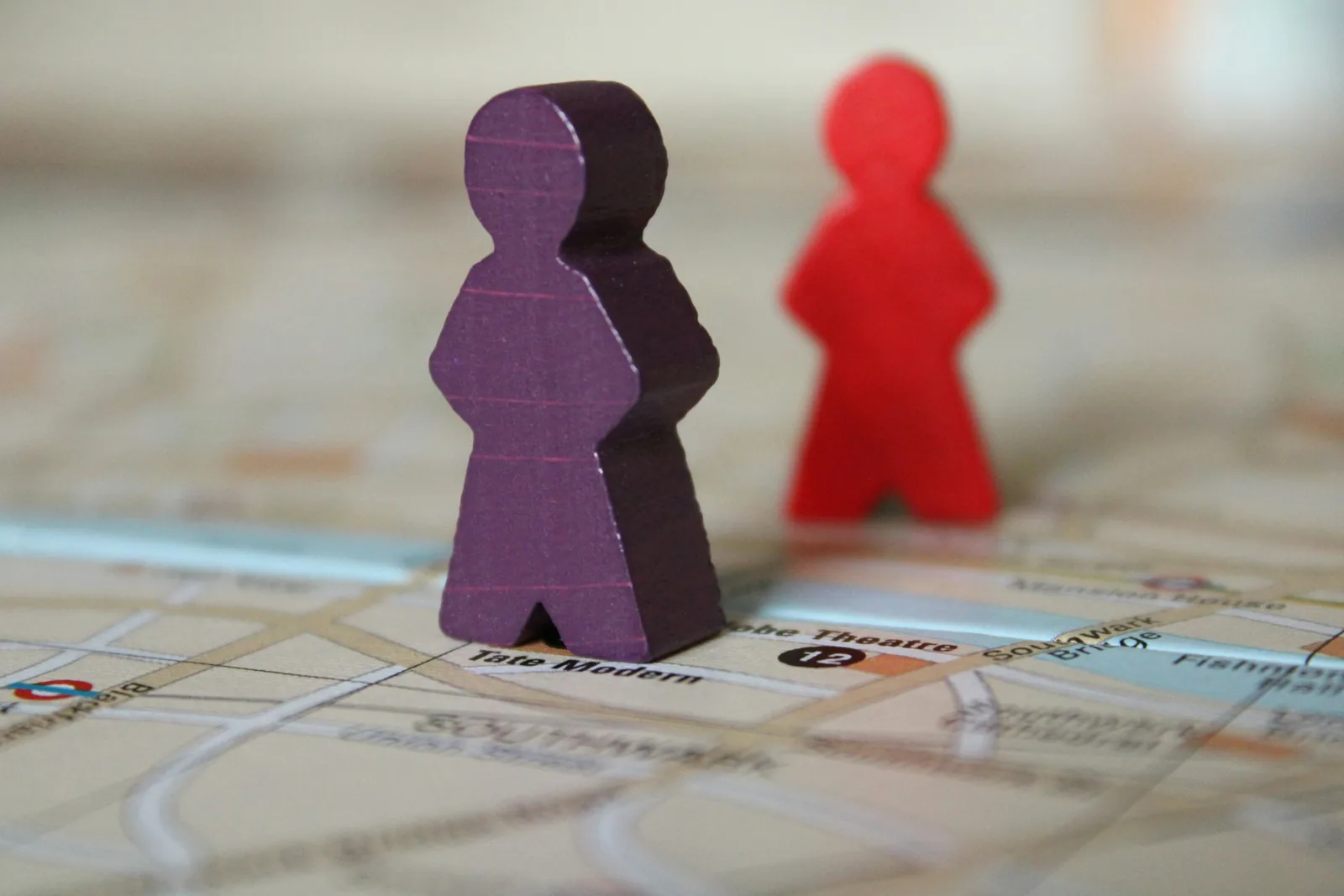 Dos figuras de madera con forma de persona sobre un mapa: una morada en primer plano y una roja, desenfocada, al fondo.